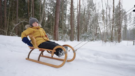 Portrait-of-a-smiling-boy-3-4-years-old-in-slow-motion-who-rides-a-sled-in-a-snowy-forest-in-winter